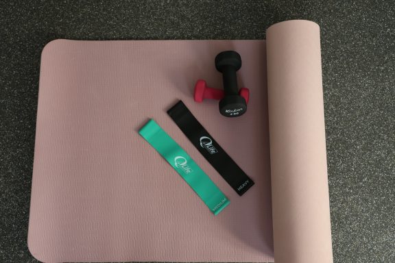 Een roze pilatesmat met dumbbell en weerstandsbanden in groen en zwart.