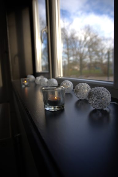 Kaarsen in glazen houders staan op een vensterbank met decoratieve elementen.