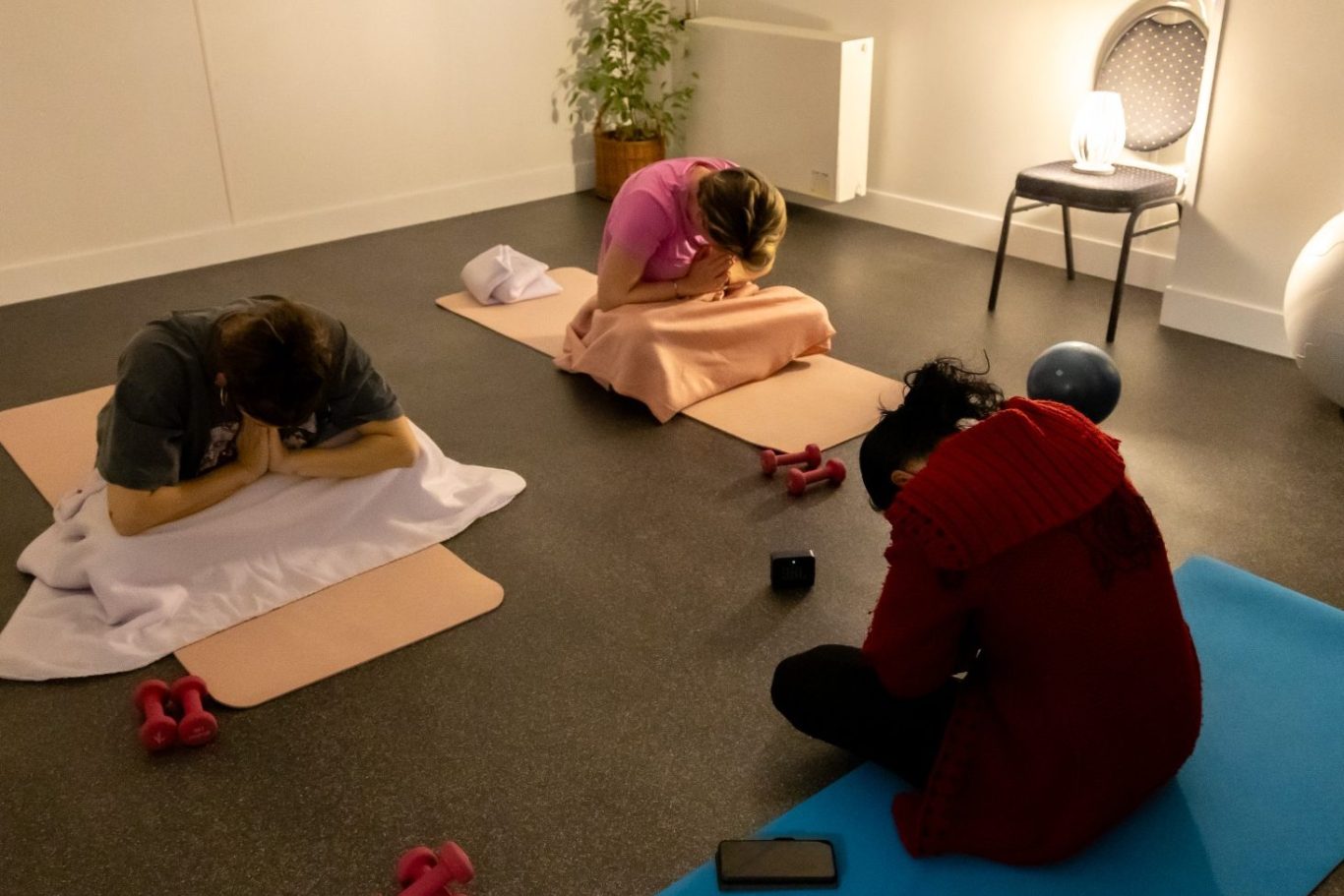 Drie personen voeren yoga-oefeningen uit op matten in een rustige ruimte.
