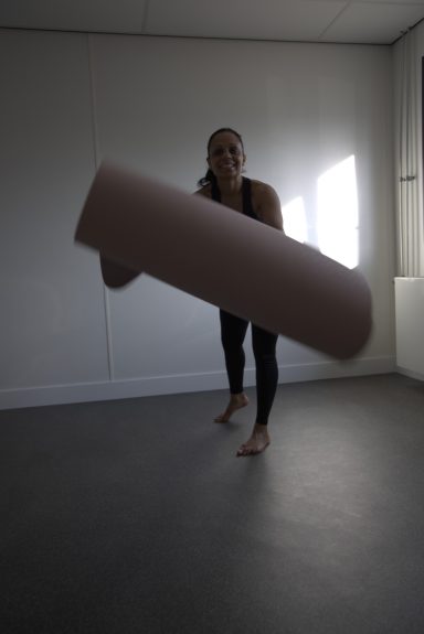 Vrouw in sportkleding houdt een grote rol van matmateriaal vast in een lichte ruimte.