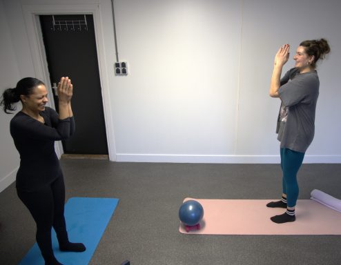 Twee vrouwen oefenen in een lichte ruimte met een fitnessbal op de vloer.